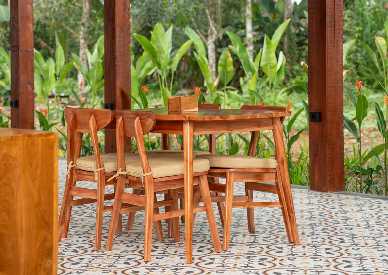 A teak table and chairs on the tiled floor, heliconia flowering just beyond the posts