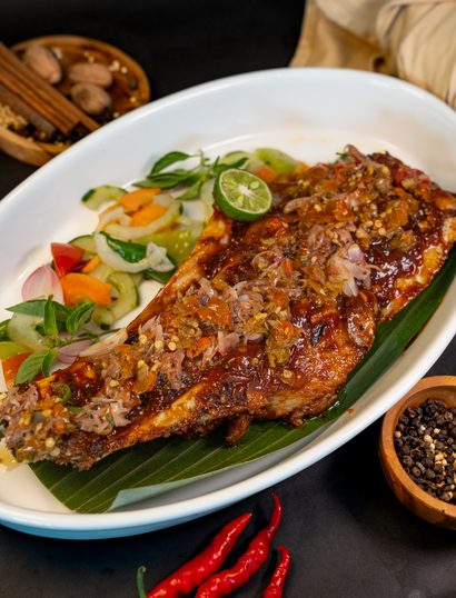 A whole fish grilled and covered in sambal, served on banana leaf with lalapan and pickles